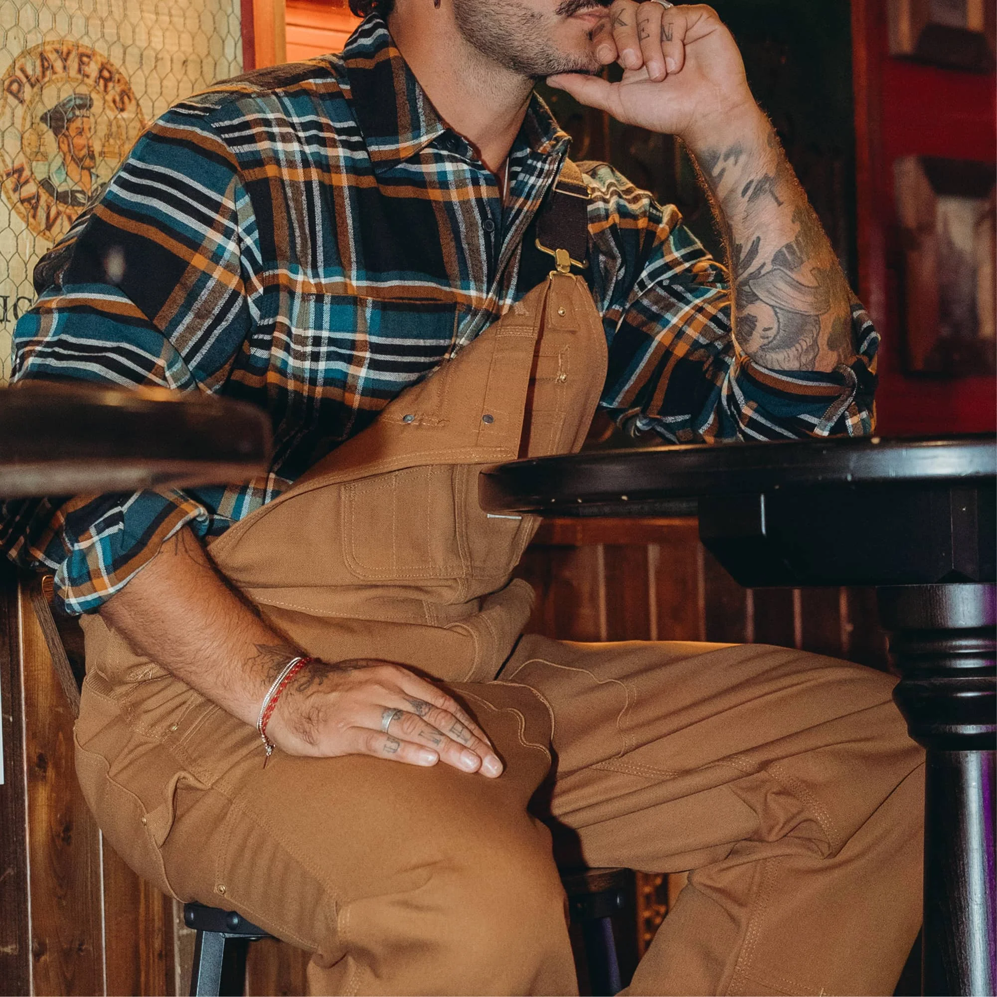 Salopette Carhartt Overall marron portée avec une chemise à carreaux, en position assise