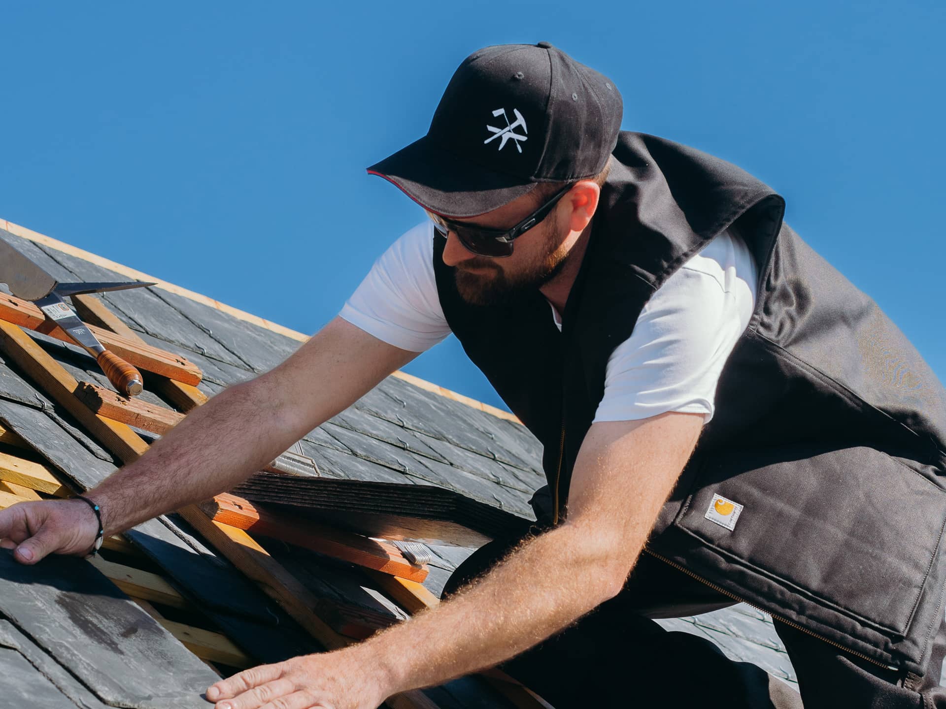 Couvreur sur un toit qui porte une casquette avec le blason des artisans couvreurs