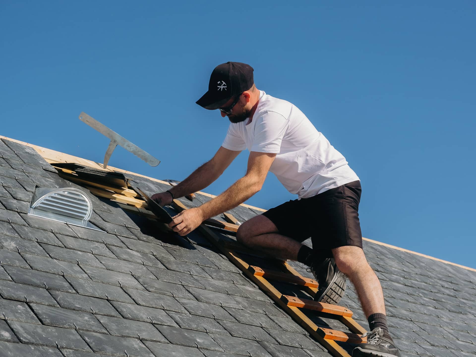Couvreur sur un toit qui travaille en short, avec une enclume de couvreur