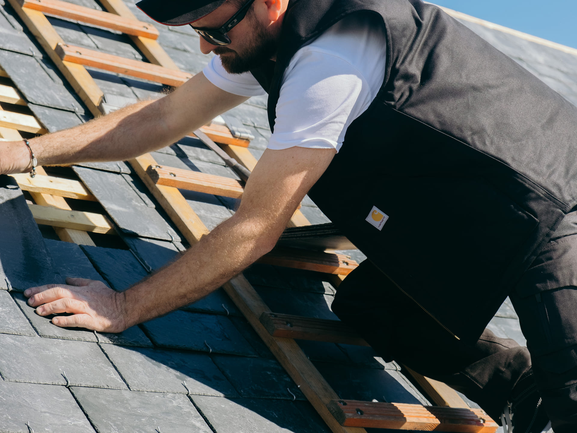 Artisan couvreur sur un toit qui porte un gilet de travail carhartt
    