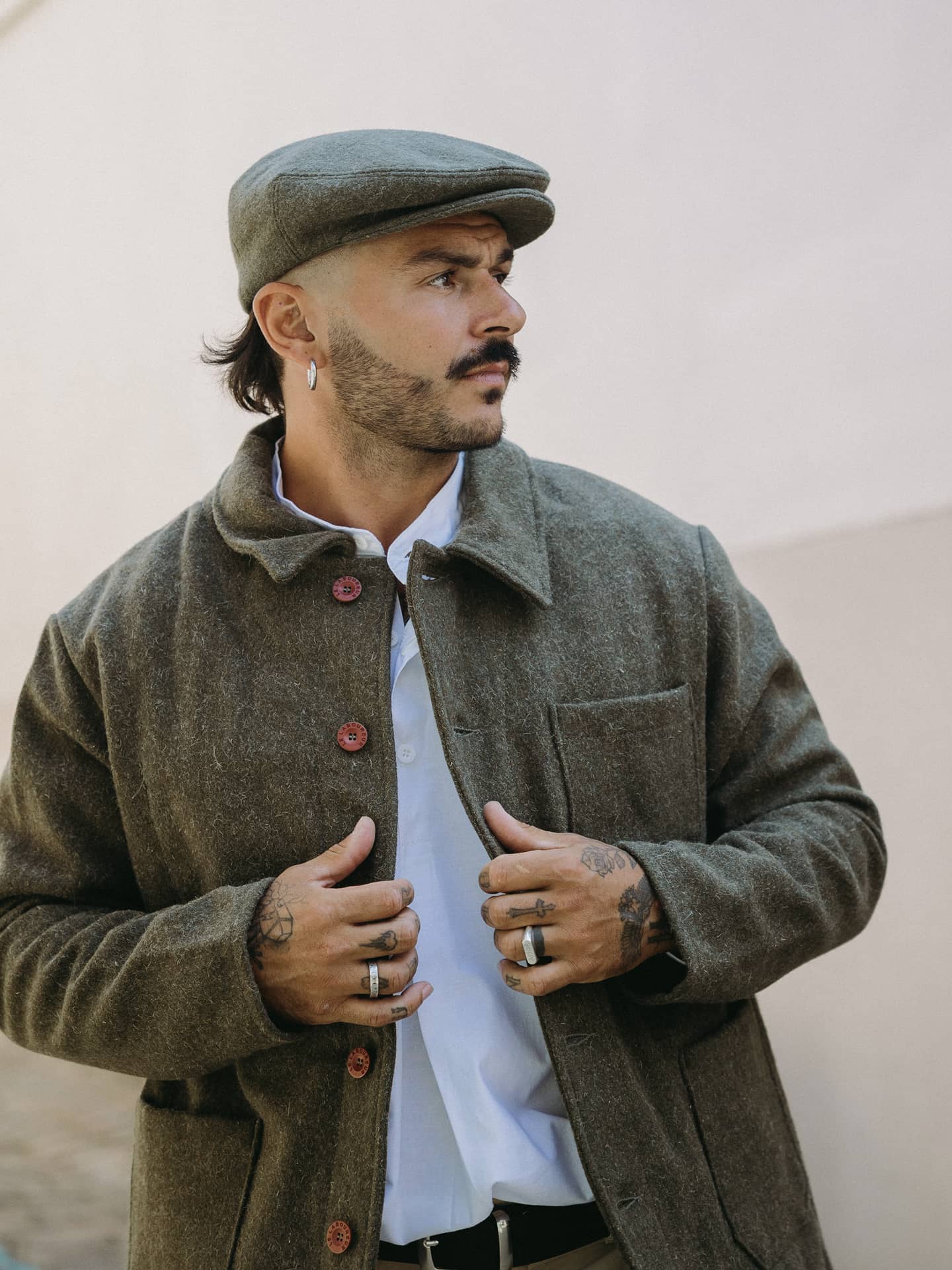 Veste en laine kaki ouverte sur une chemise blanche à col officier, avec casquette en laine assortie