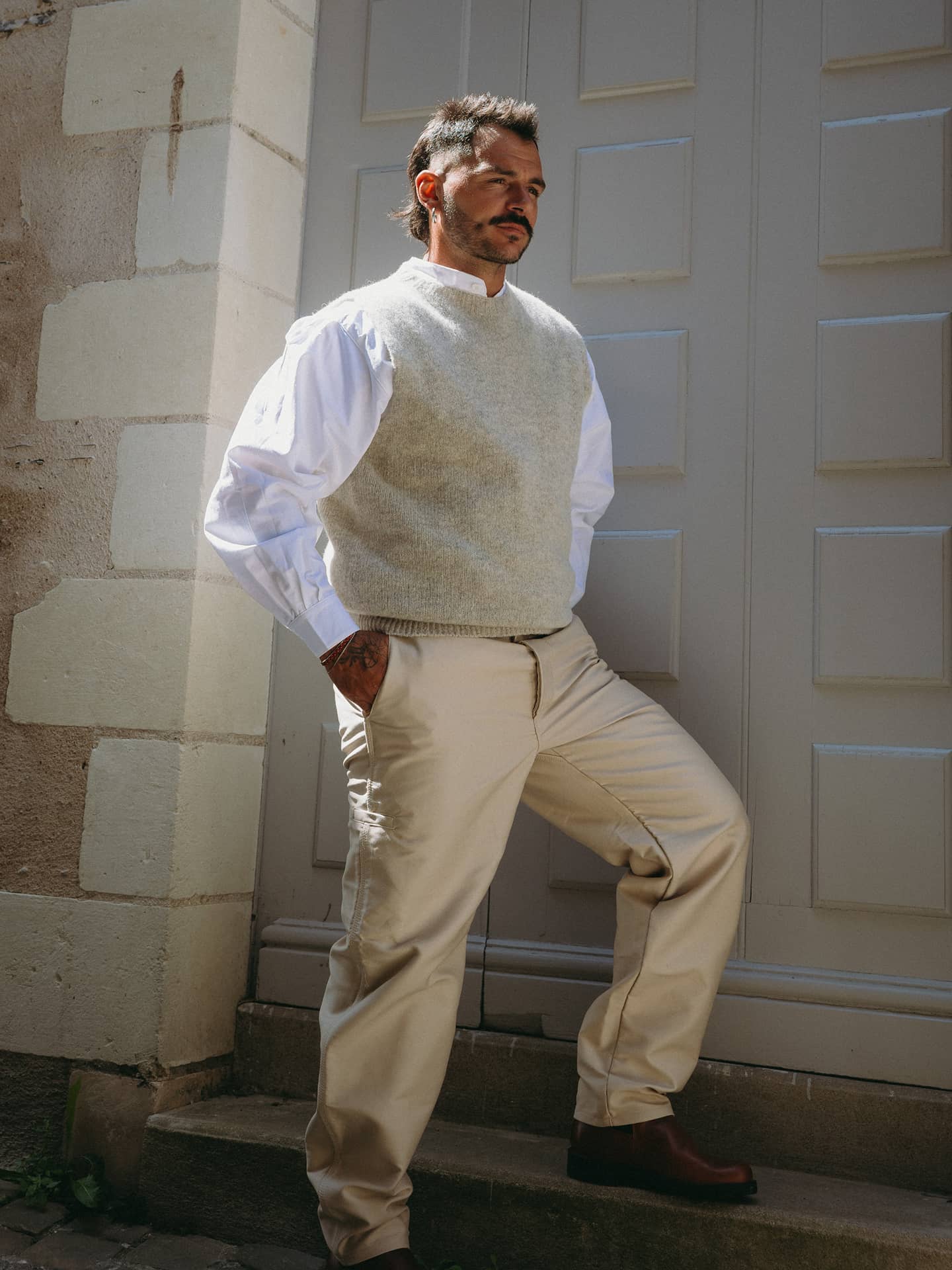 Silhouette complète avec pull sans manches, chemise blanche, largeot écru et boots en cuir brun